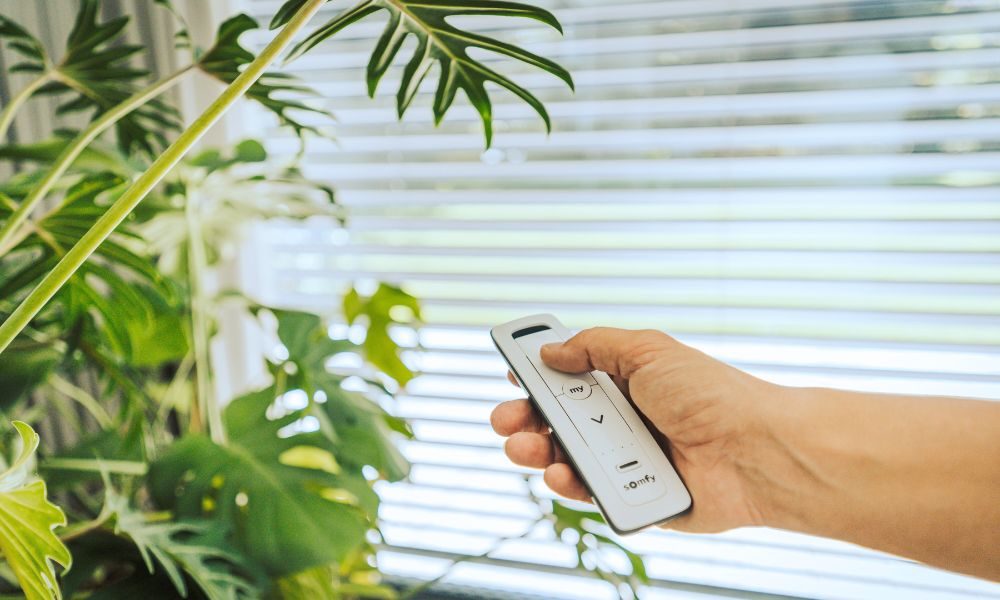 Person hält SOMFY Fernbedienung in der Hand, im Hintergrund: Raffstore